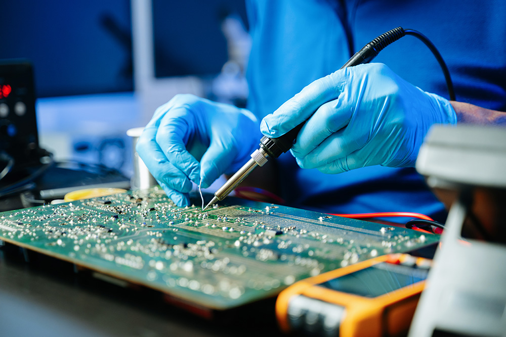 Closeup of expert soldering a green PCB board using precision tools