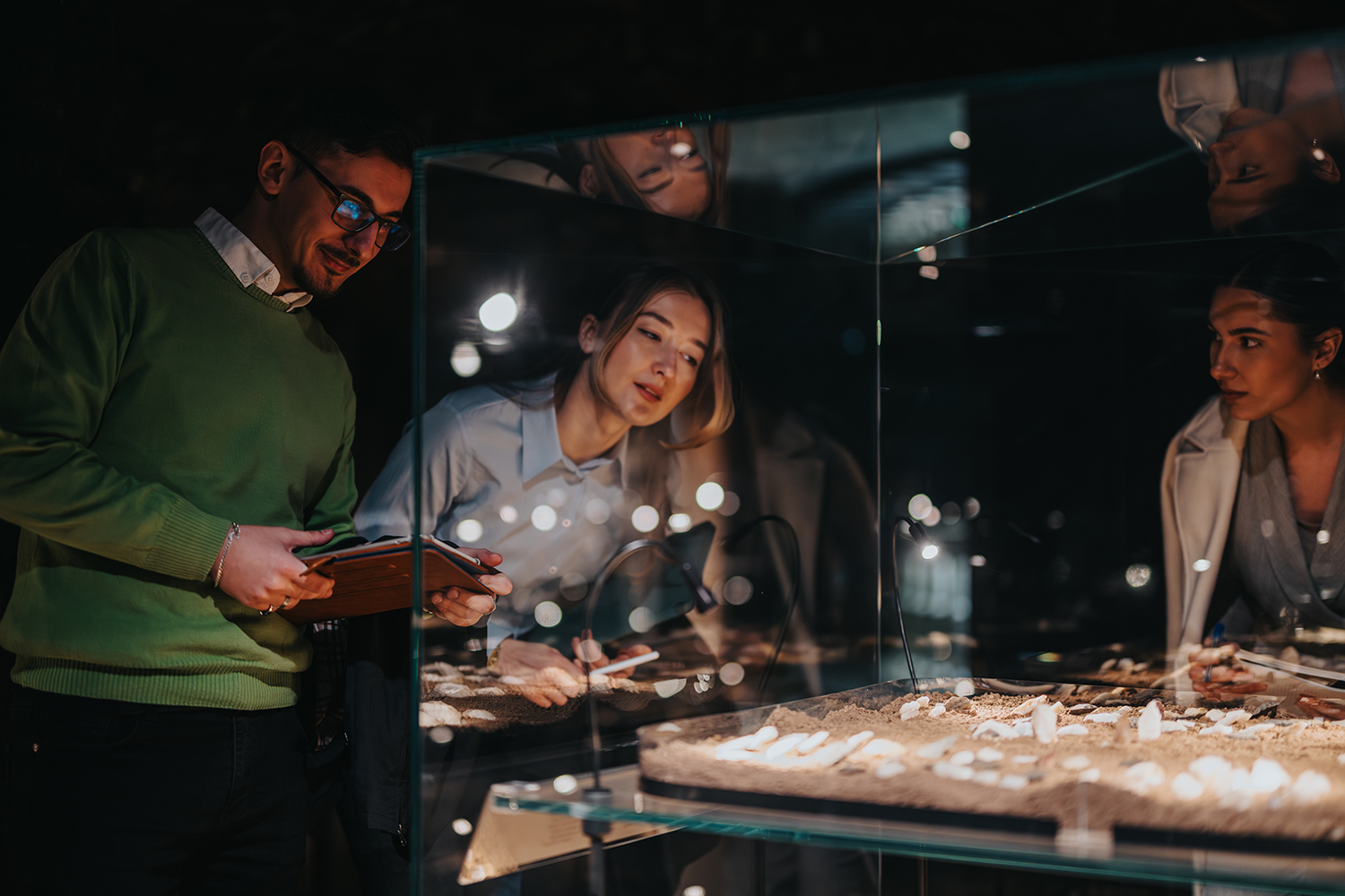Three people exploring artifacts in a clear display case in a museum